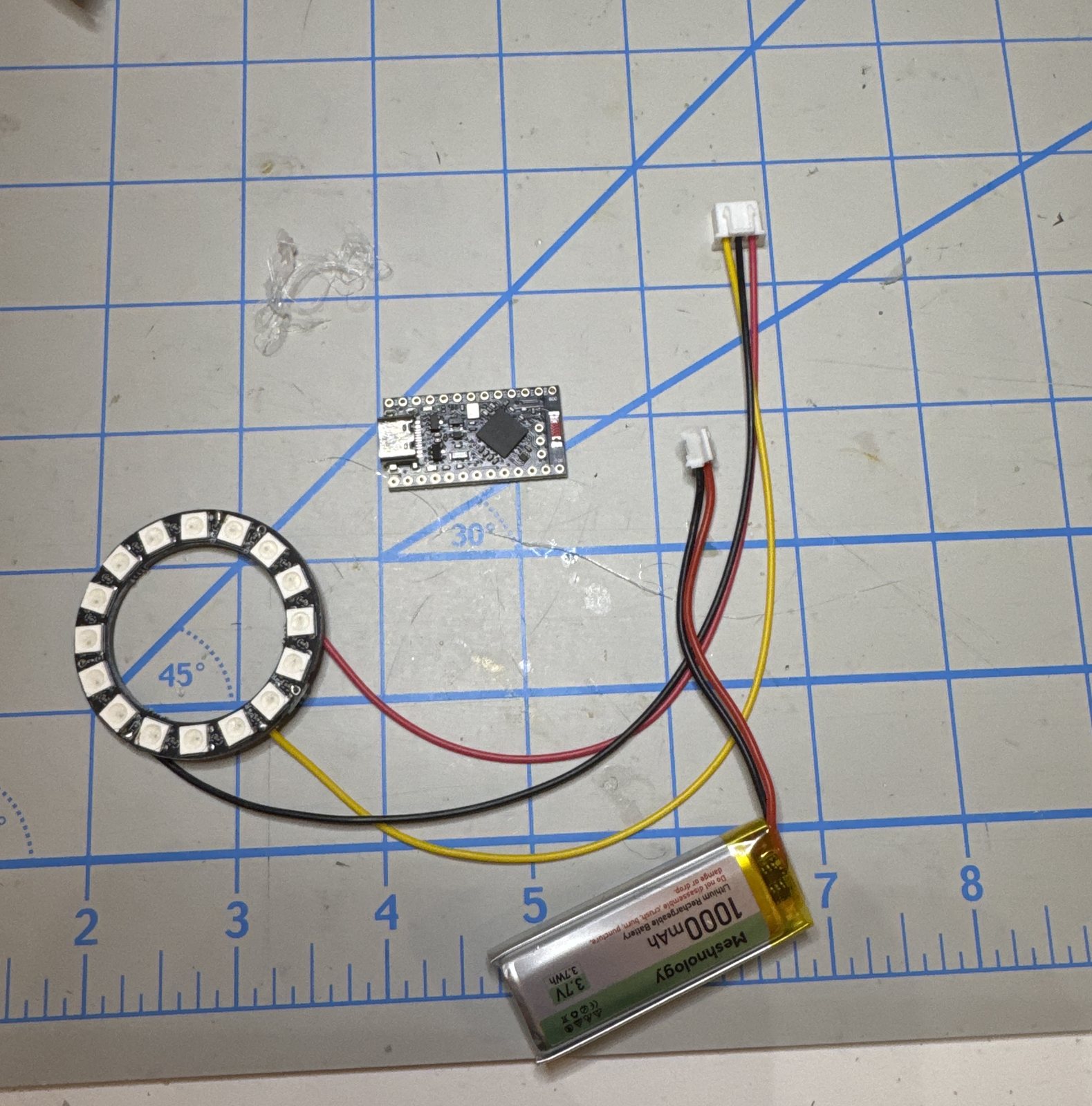 A 16-LED ring, an nRF52840 module and a 1000 mAh cell laid out on a cutting mat