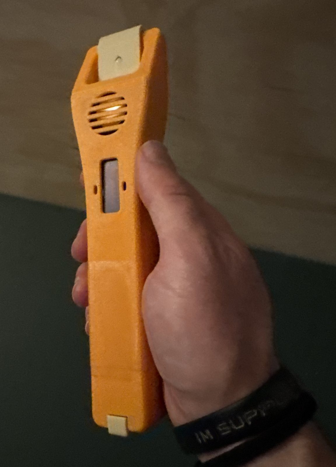 A handheld scanner in an orange printed case, held in one hand